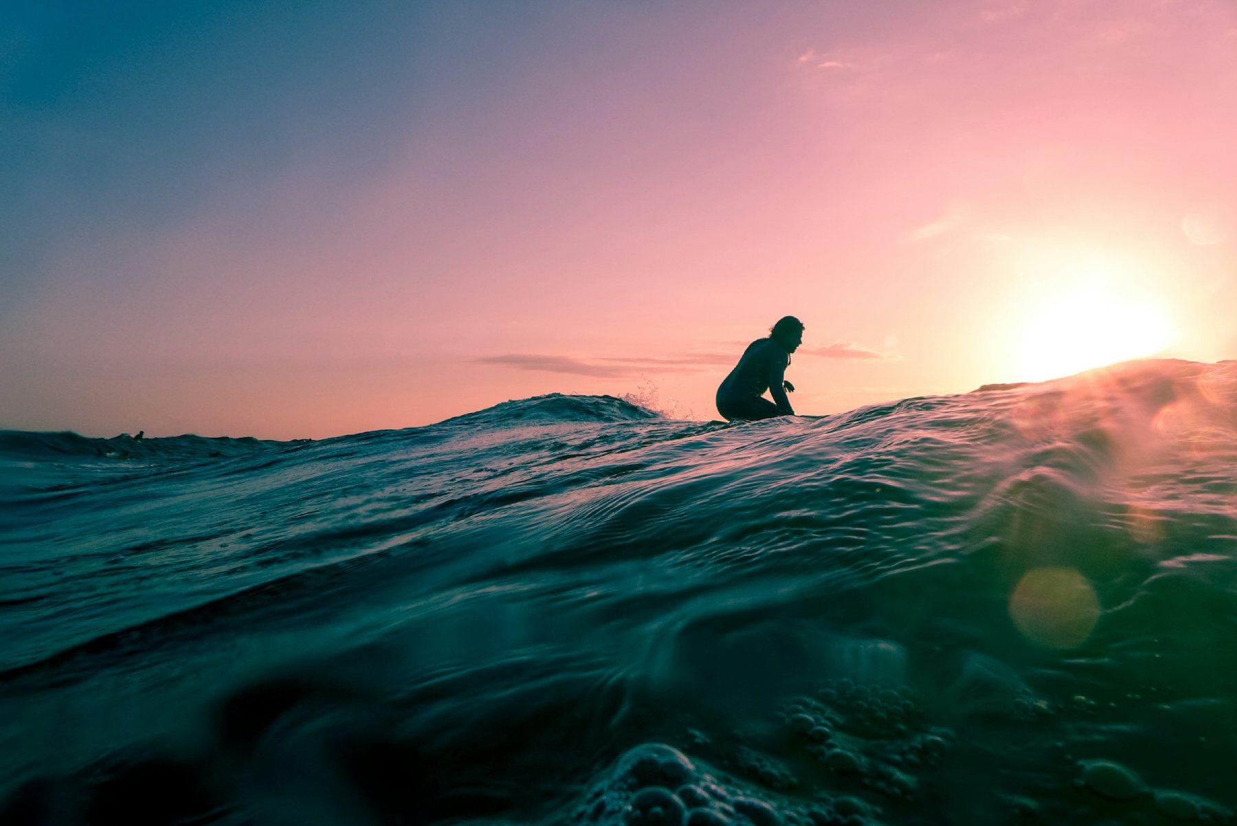 Surfista surfeando en la puesta de sol visto desde atras con colores suaves